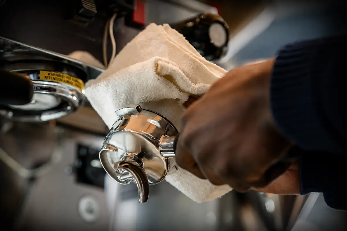 Cleaning an espresso portafilter with a microfiber cloth to remove coffee oils and residue after brewing.
